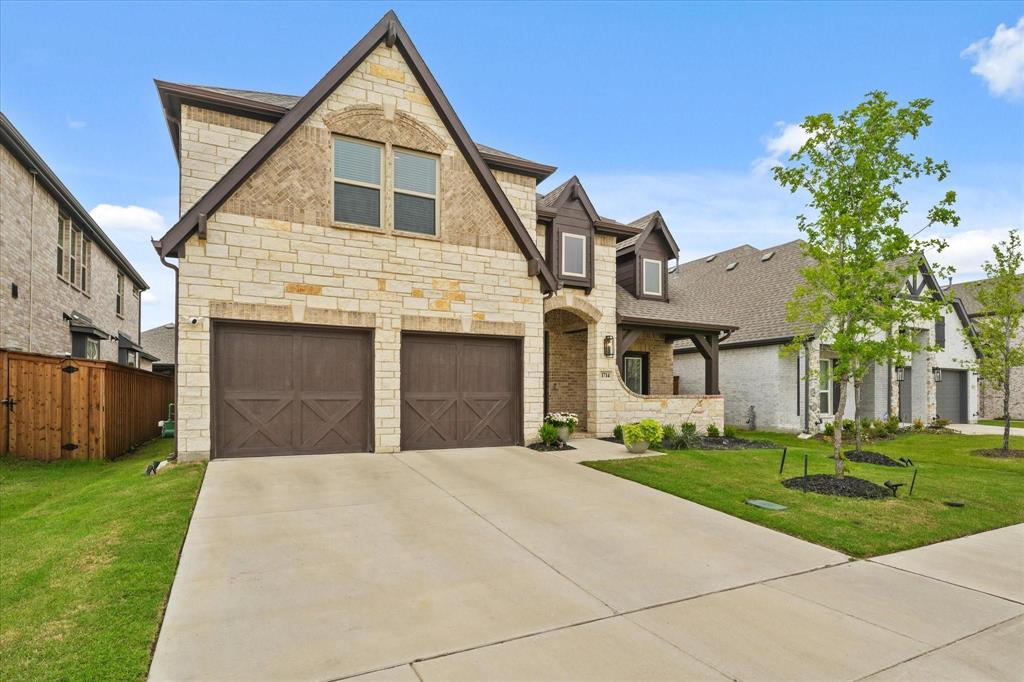 1714 Highwood Road Forney, TX 75126 - Photo 2 of 28 French country style house featuring stone siding, a front lawn, an attached garage, concrete driveway, and a shingled roof