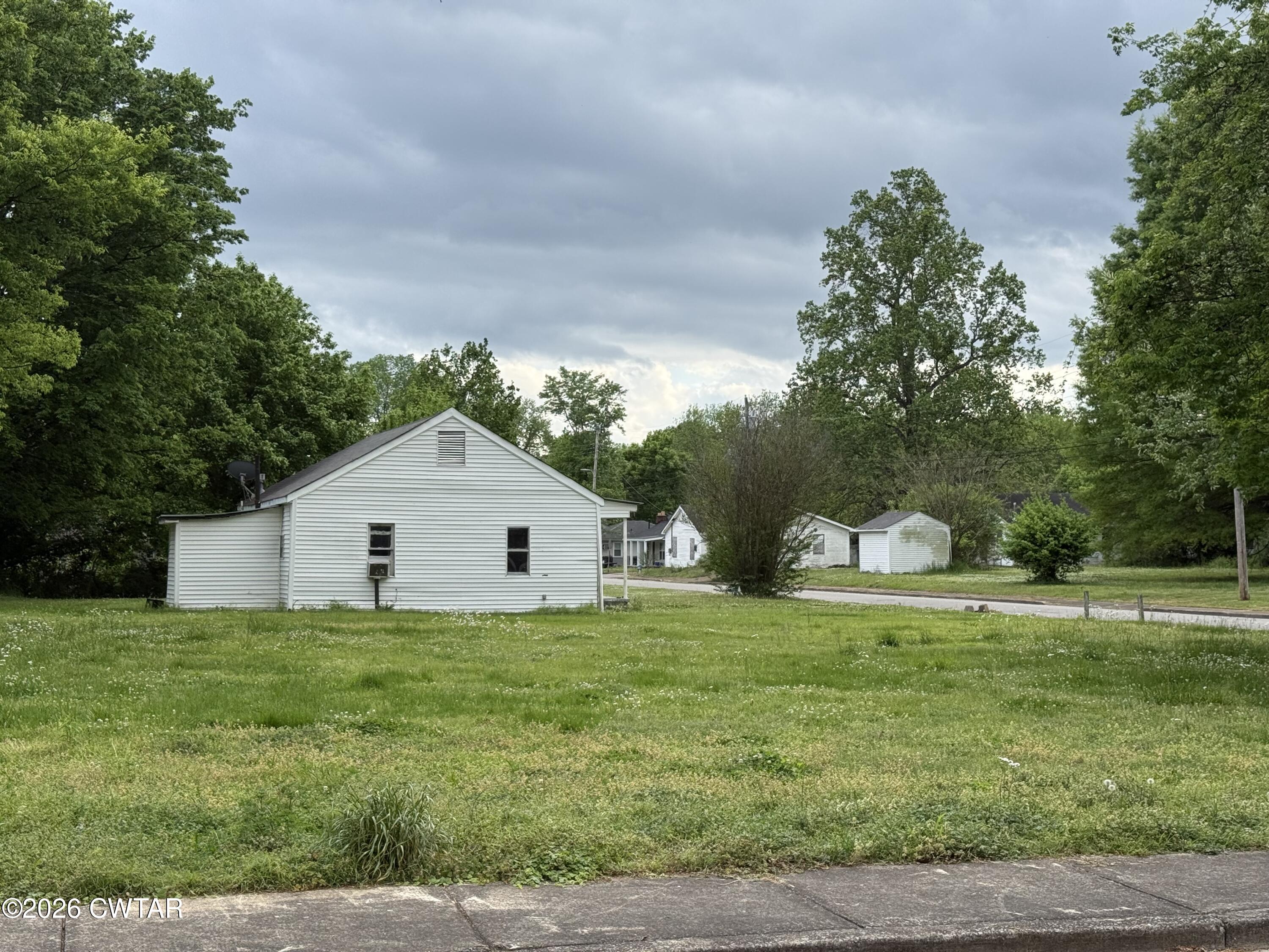 a white house with a big yard and large trees with wooden fence