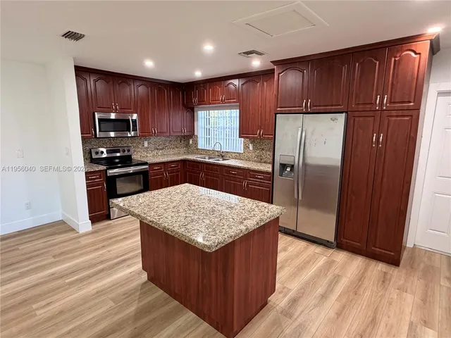a kitchen with stainless steel appliances granite countertop wooden cabinets a refrigerator and a sink