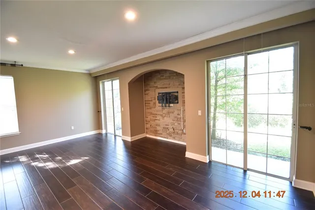 a view of an empty room and kitchen with hardwood floor