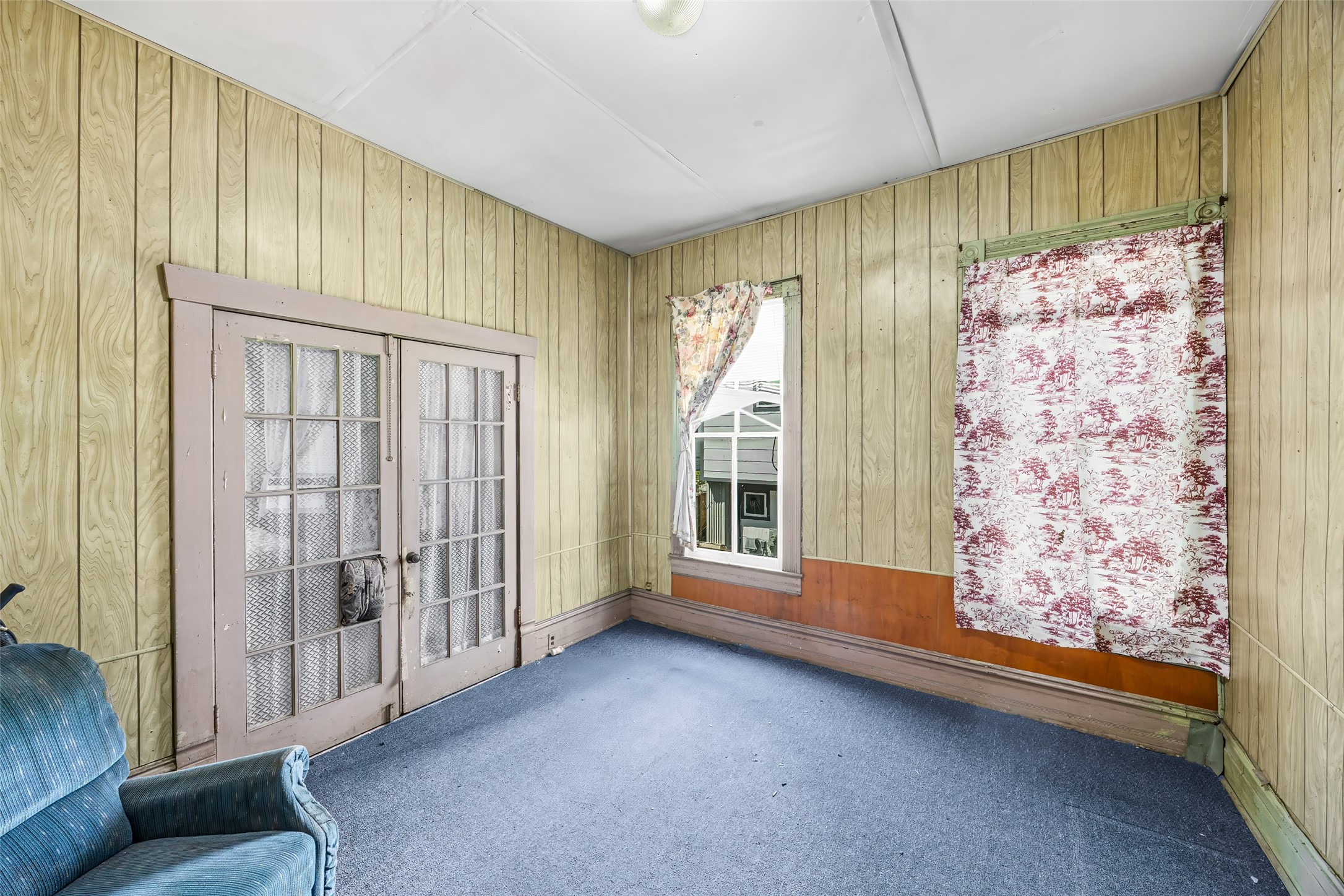 1214 Edwards Street Houston, TX 77007 - Photo 12 of 34 This room features wood panel walls and carpeted flooring, with natural light coming through large windows. It includes a set of French doors and has potential for updating to suit personal taste.