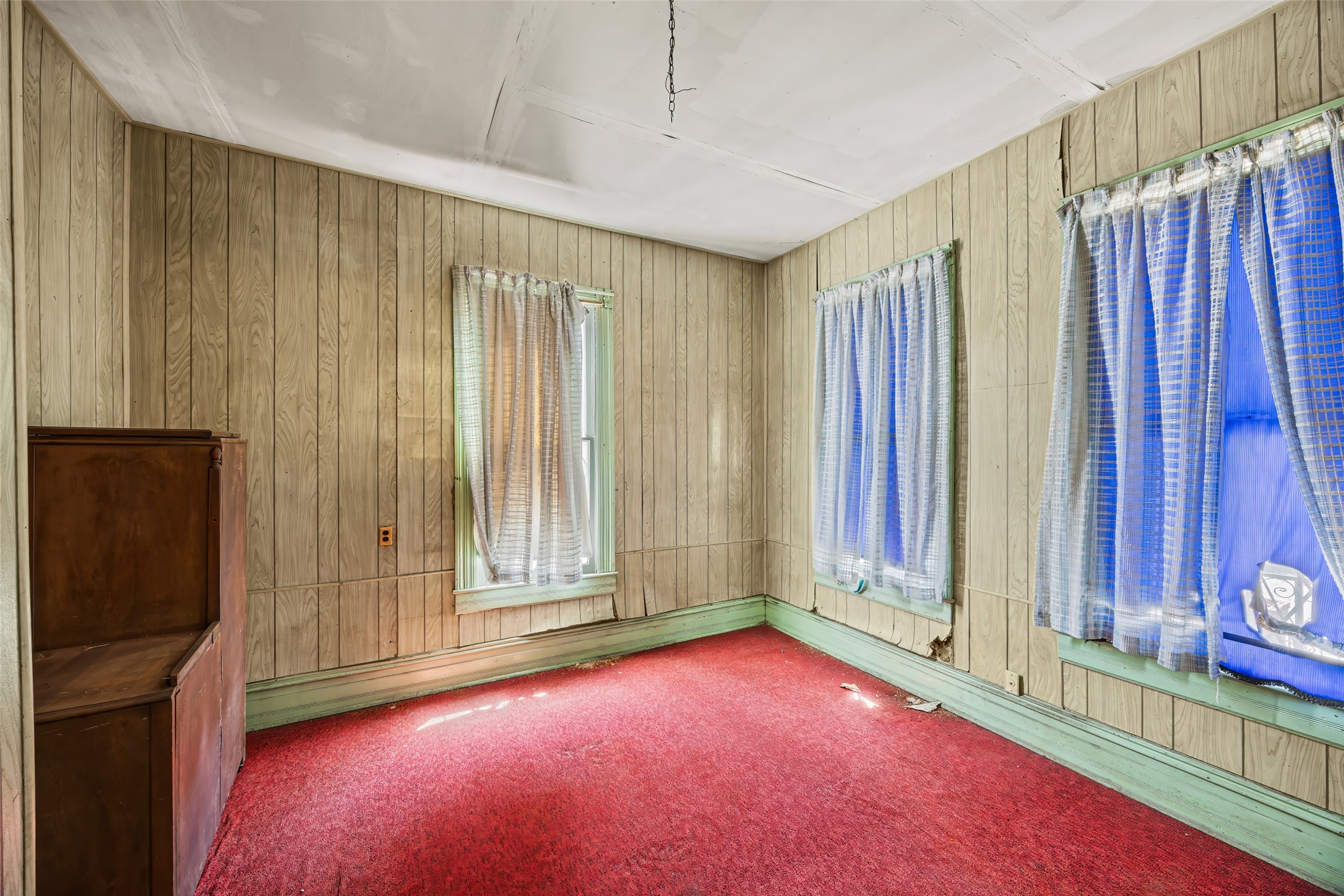 1214 Edwards Street Houston, TX 77007 - Photo 16 of 34 A cozy room with vintage wood paneling, red carpet, and two windows with sheer curtains. It has potential for renovation and personalization.