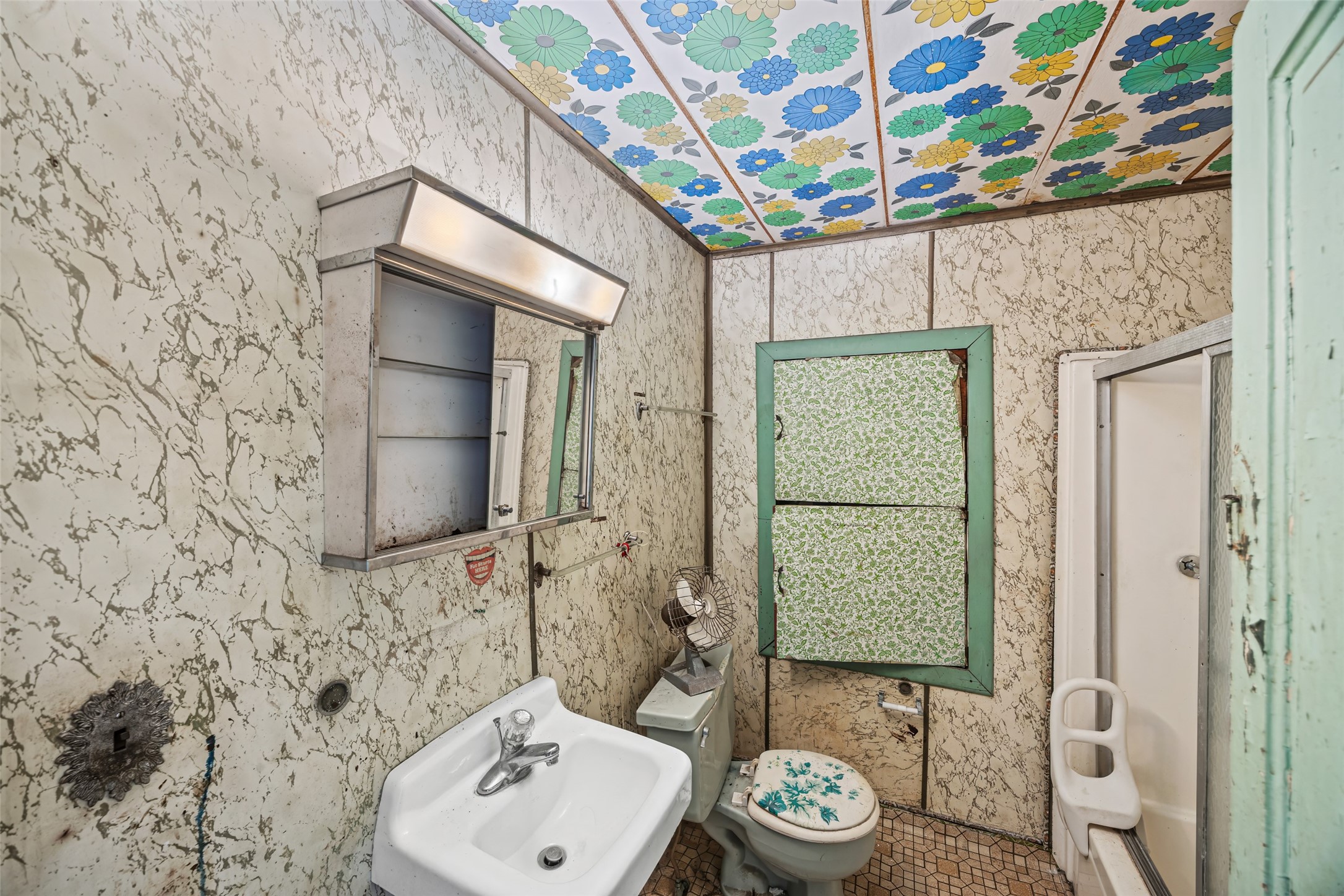 1214 Edwards Street Houston, TX 77007 - Photo 17 of 34 This is a compact bathroom with vintage charm, featuring a colorful floral ceiling, patterned walls, and basic fixtures including a small sink, toilet, and shower. Ideal for renovation potential.