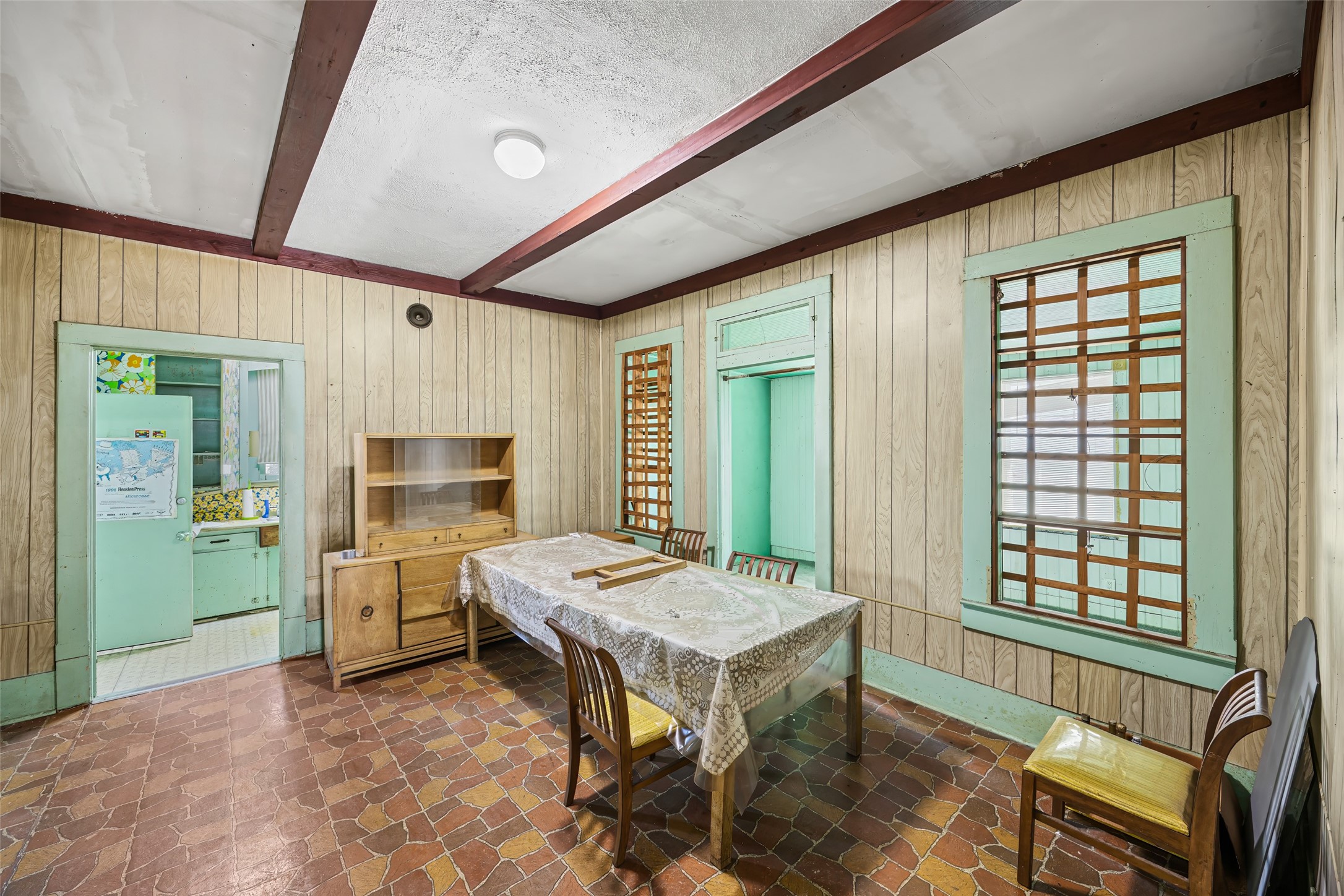 1214 Edwards Street Houston, TX 77007 - Photo 18 of 34 This room features wood panel walls and a tiled floor, with exposed beams on the ceiling. It includes a dining table and chairs, a wooden cabinet, and windows with decorative grilles, creating a rustic, vintage atmosphere.