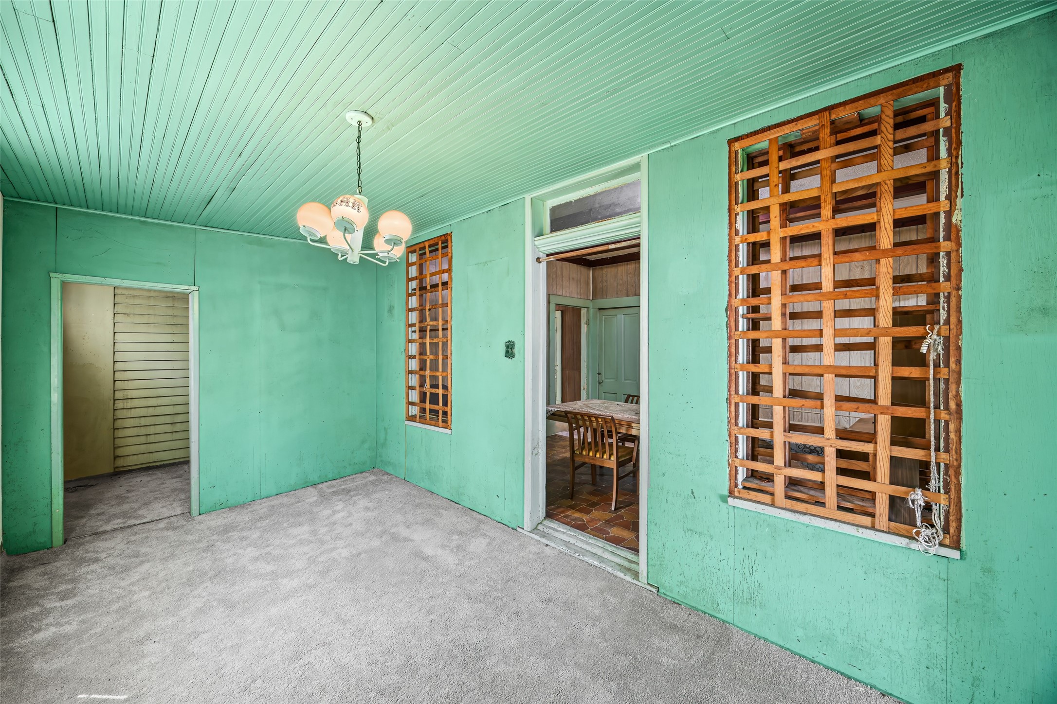 1214 Edwards Street Houston, TX 77007 - Photo 19 of 34 This room features mint green walls and ceiling, with a unique wooden lattice window. It has an overhead chandelier and connects to another room through an open doorway. The space is carpeted, offering a cozy feel.