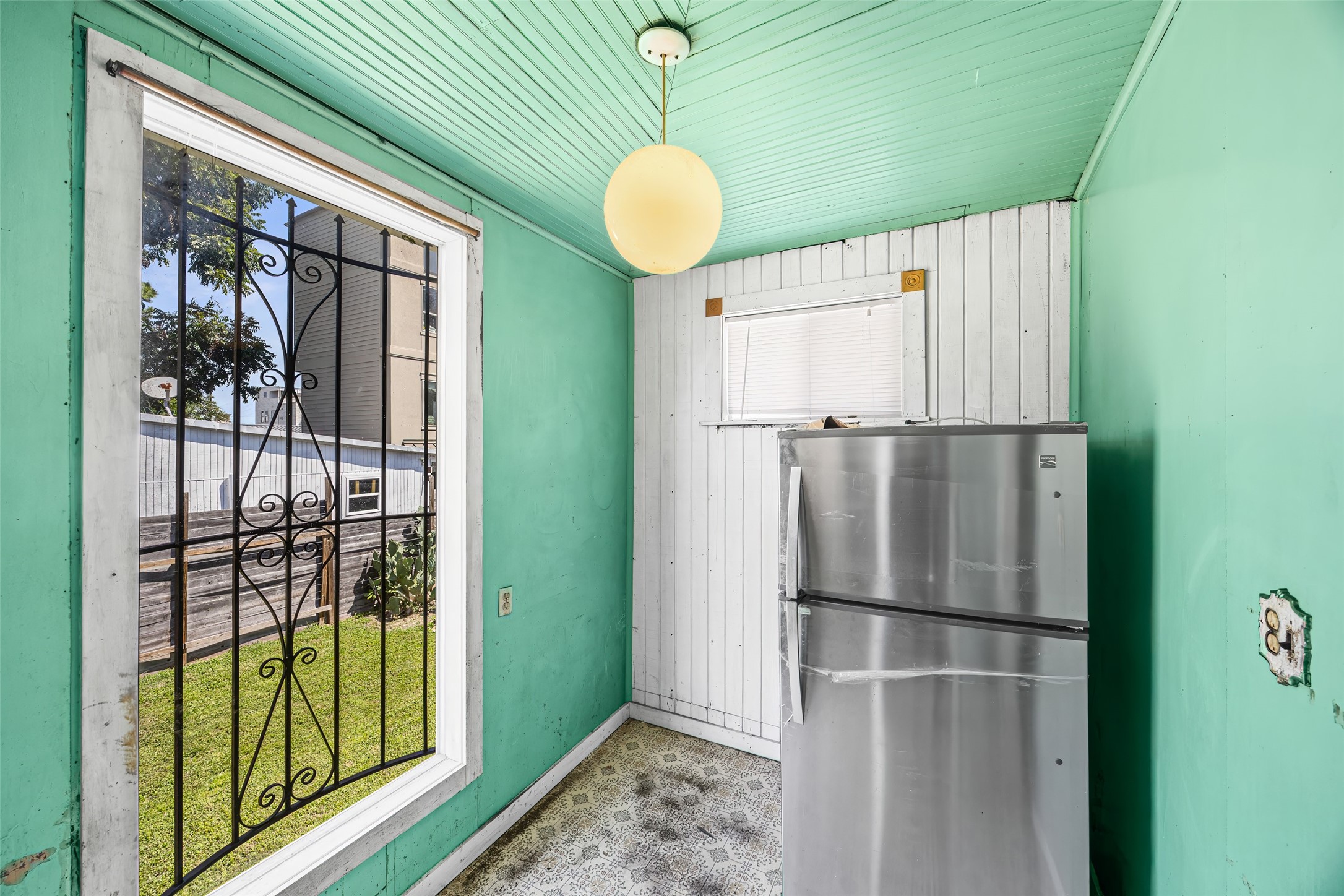 1214 Edwards Street Houston, TX 77007 - Photo 21 of 34 This small, enclosed space features a bright green interior with a vintage feel, including a patterned floor and a pendant light. It has a large window with decorative iron bars and houses a stainless steel refrigerator.