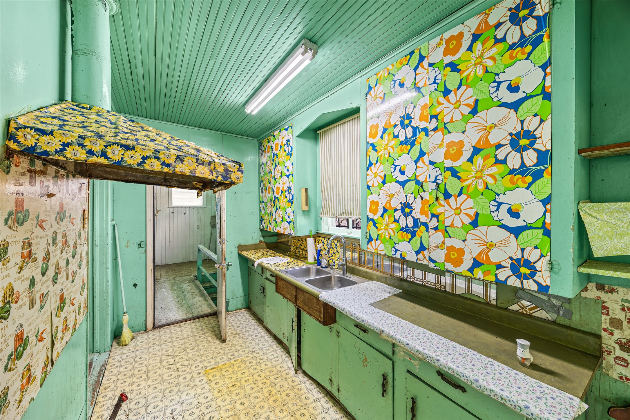 1214 Edwards Street Houston, TX 77007 - Photo 22 of 34 This vibrant, vintage kitchen features bold floral wallpaper and colorful cabinetry, offering a retro charm. It includes a double sink, ample counter space, and a unique awning feature, perfect for those who appreciate a nostalgic aesthetic.