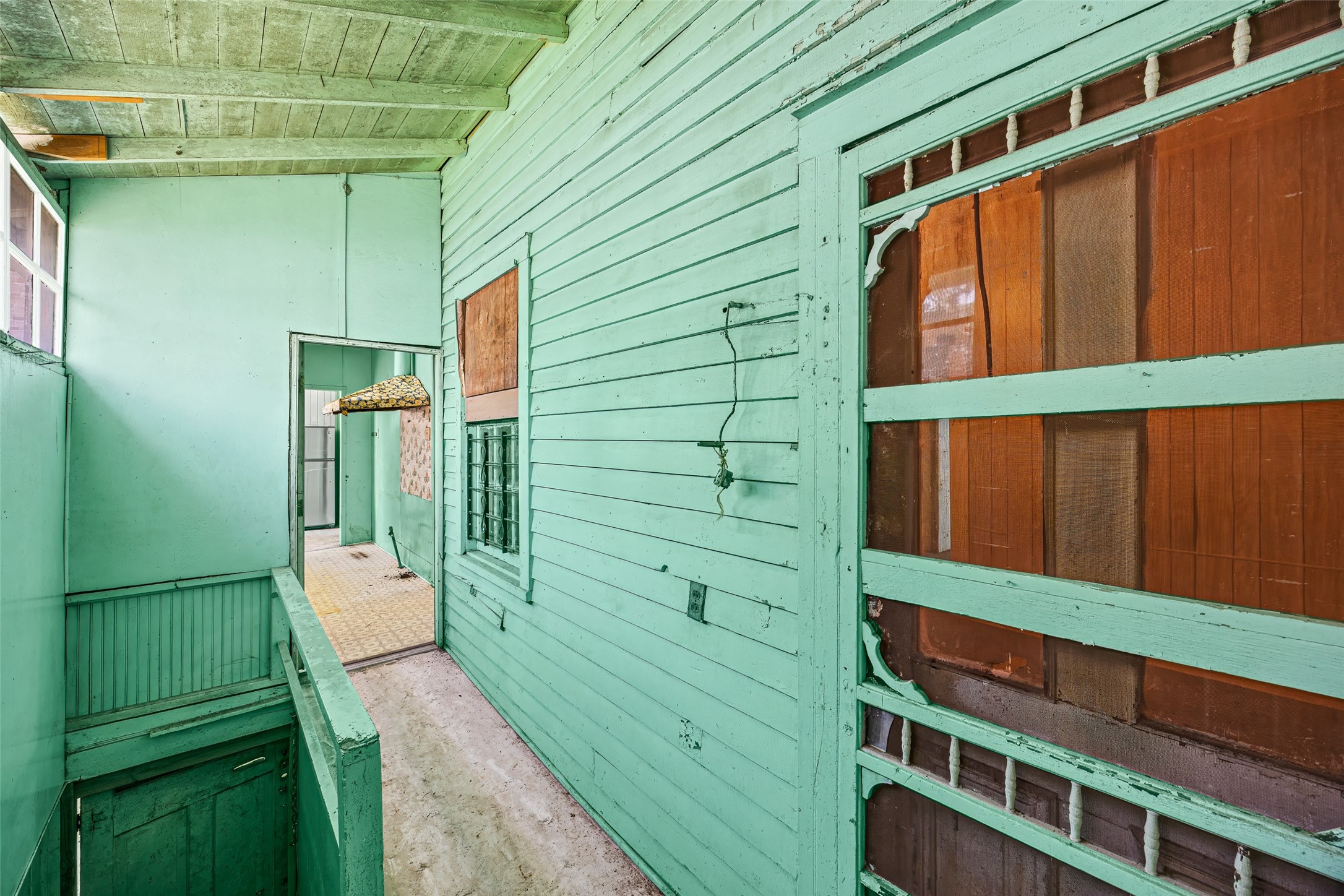 1214 Edwards Street Houston, TX 77007 - Photo 23 of 34 This is a rustic, enclosed porch area with a vintage vibe. The walls and ceiling are painted in a mint green color, featuring wooden paneling and a visible staircase leading down. The space has potential for renovation and customization.