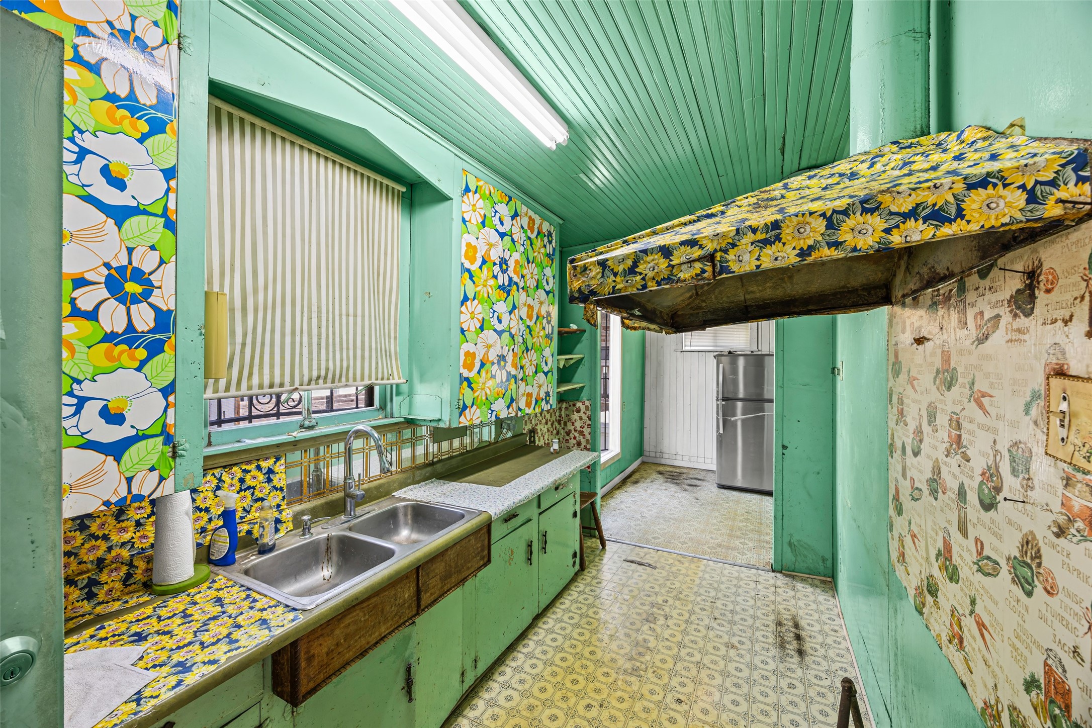 1214 Edwards Street Houston, TX 77007 - Photo 24 of 34 This kitchen features a retro vibe with vibrant floral wallpaper and mint green cabinetry. It includes a double sink, a vintage-style range hood, and a small dining area. The space is colorful and unique, appealing to those seeking a distinctive design.