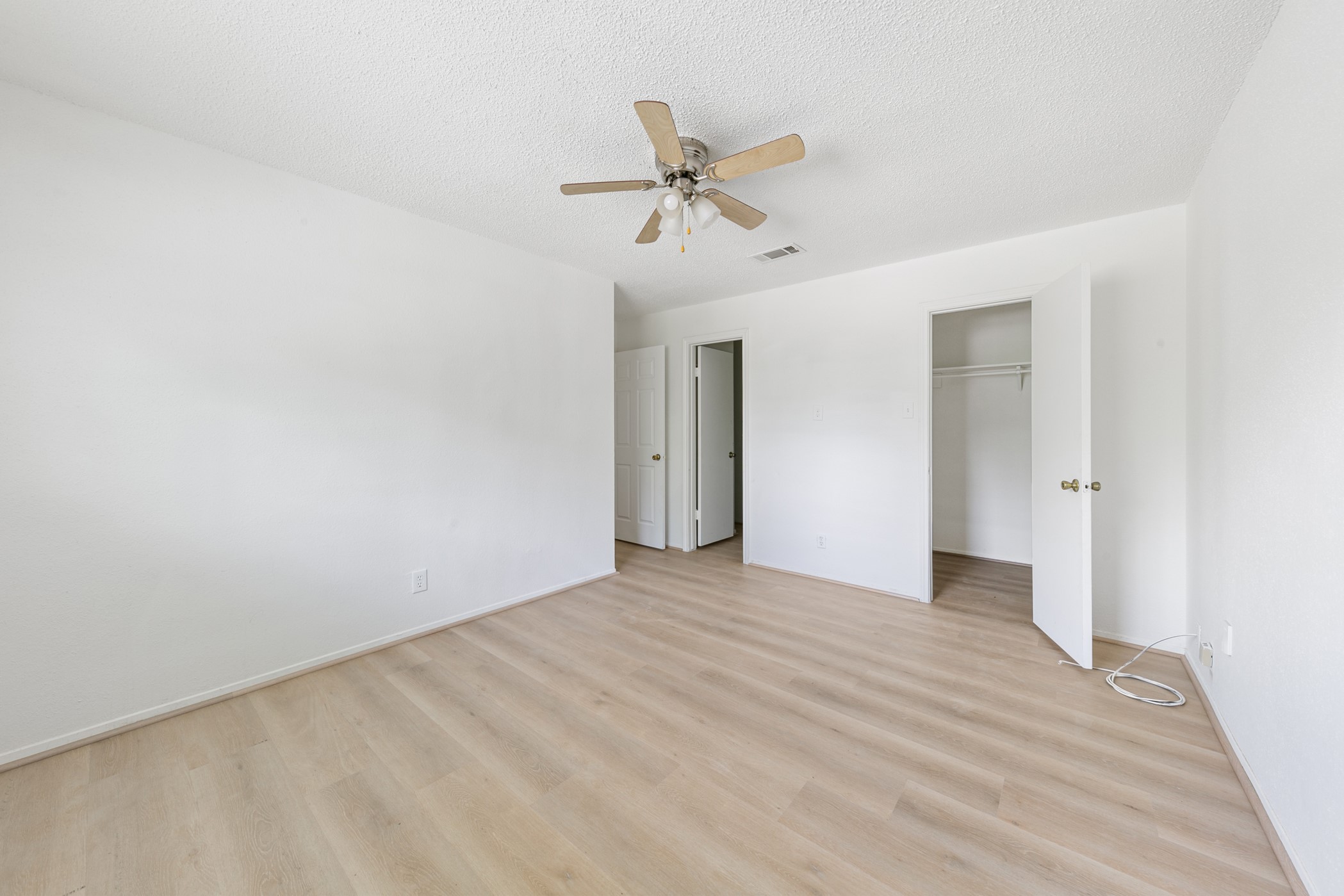 700 Lyle W Avenue, Unit D Cleveland, TX 77327 - Photo 13 of 16 This is a bright, spacious bedroom with light wood flooring, white walls, and a ceiling fan. It features a closet with a door and ample space for furnishings.