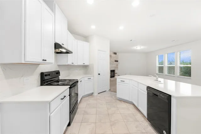 a large white kitchen with stainless steel appliances granite countertop a stove a sink a refrigerator and white cabinets with wooden floor