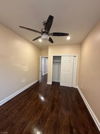 a view of an empty room with wooden floor and a ceiling fan
