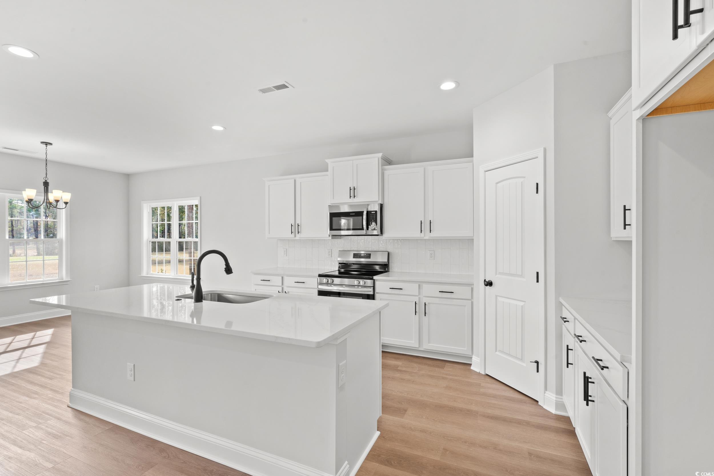 908 Francis Parker Road Georgetown, SC 29440 - Photo 5 of 37 Kitchen featuring a center island with sink, backsplash, appliances with stainless steel finishes, white cabinets, and hanging light fixtures