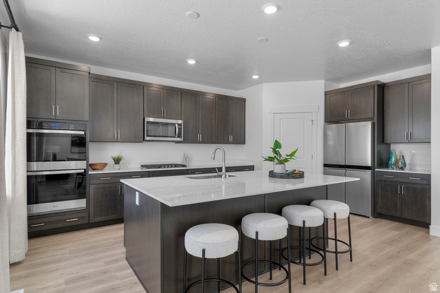 1418 West 2350th South, Unit 15 Perry, UT 84302 - Photo 8 of 22 Contemporary kitchen featuring a large central island with seating, dark wood-finish cabinetry, stainless steel appliances, and light wood-finish flooring