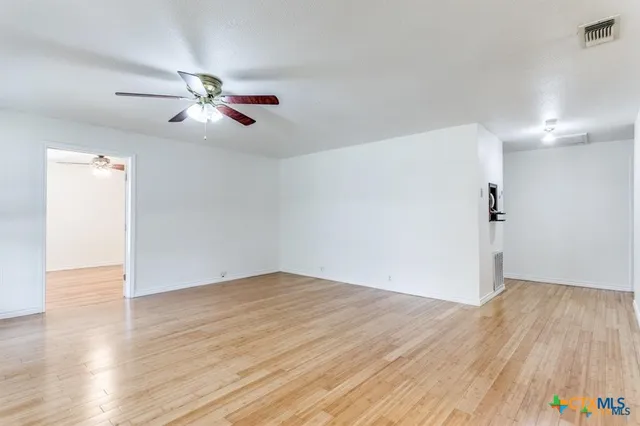 a view of empty room with wooden floor and ceiling fan