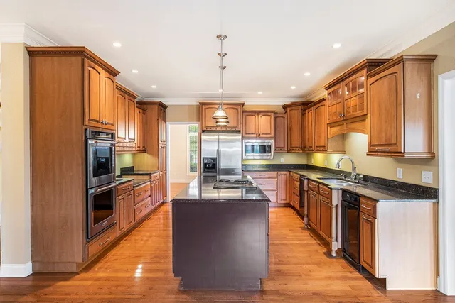 a kitchen with stainless steel appliances granite countertop a refrigerator a sink dishwasher a stove and a dining table with wooden floor