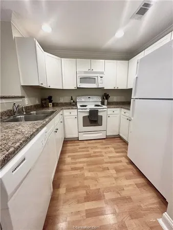 a large white kitchen with granite countertop a sink a stove a refrigerator and white cabinets