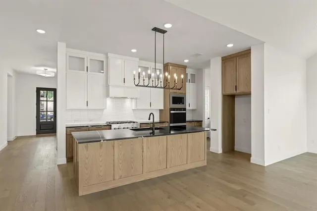 a kitchen with stainless steel appliances granite countertop a sink a stove a refrigerator and island with wooden floor