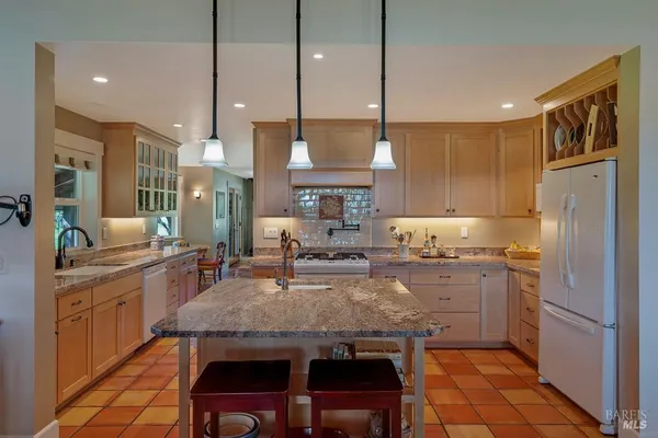 a kitchen with kitchen island granite countertop a table chairs sink refrigerator and cabinets