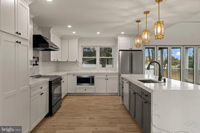 a kitchen with stainless steel appliances granite countertop a stove top oven a sink dishwasher a refrigerator and a dining table with wooden floor