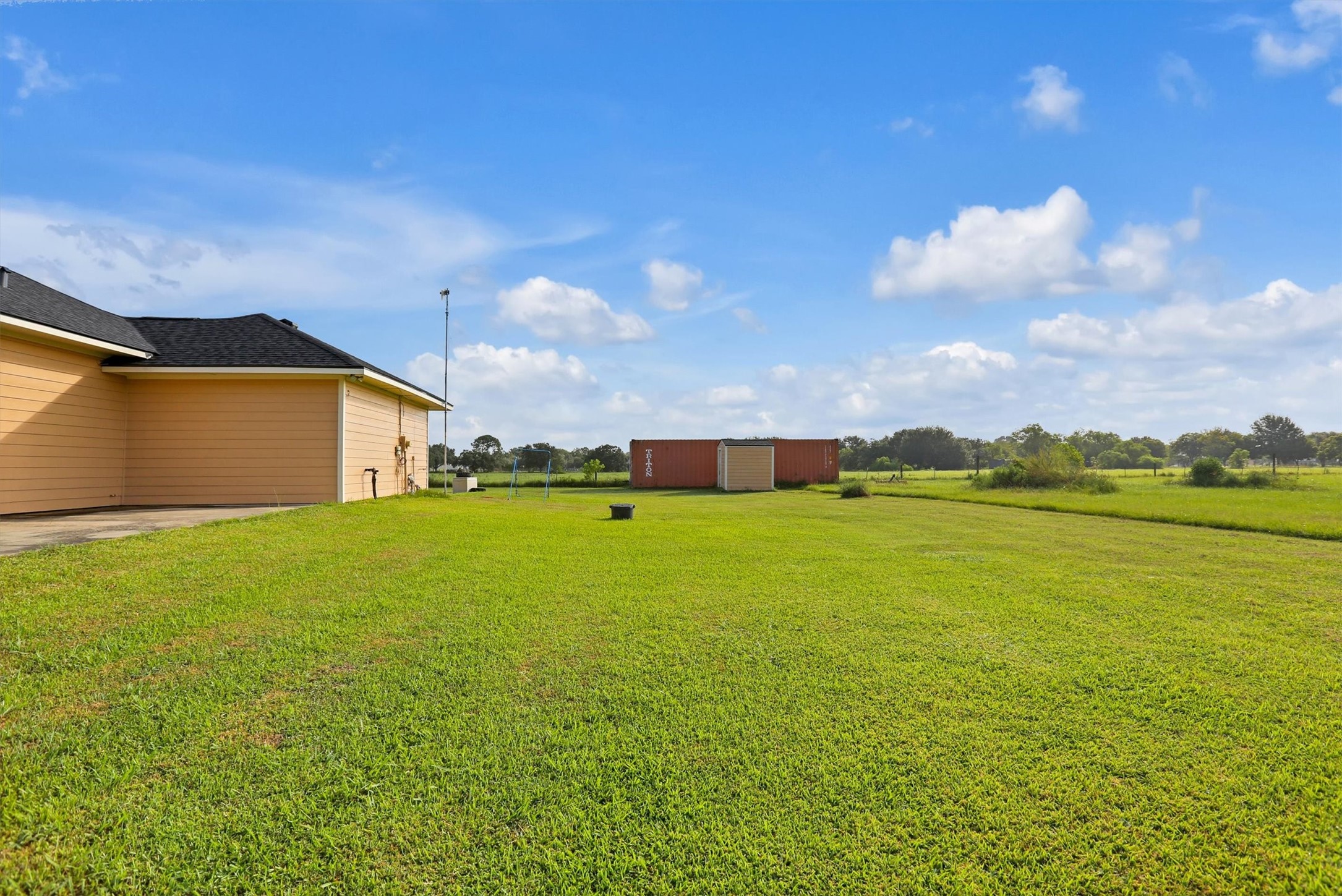 8131 Brinkmeyer Road Needville, TX 77461 - Photo 15 of 49 Expansive backyard with a well-maintained lawn, perfect for outdoor activities and relaxation, set against a backdrop of open skies and serene countryside views.