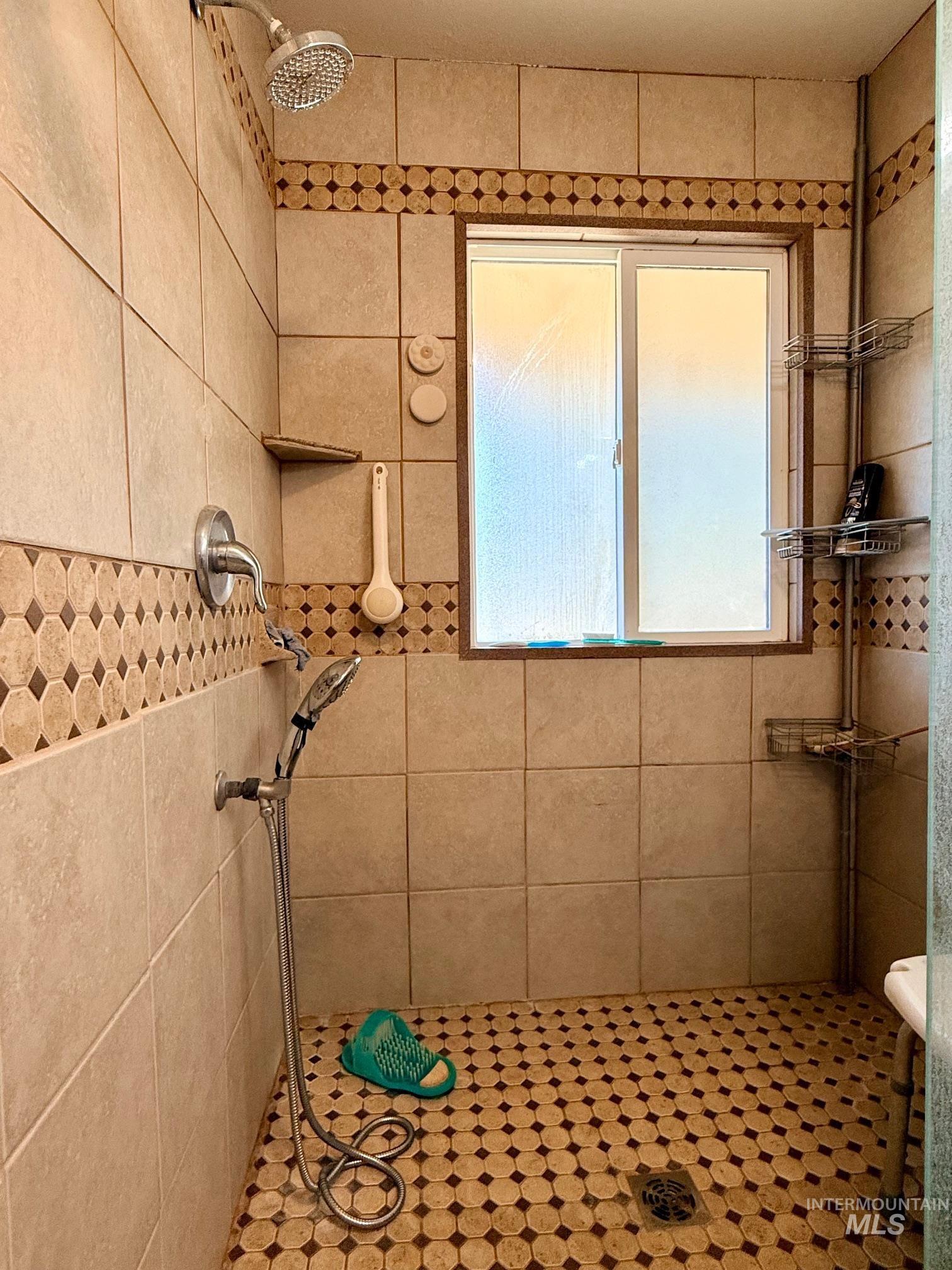 35322 River Road Lenore, ID 83541 - Photo 20 of 42 Tiled shower with a frosted window, featuring a fixed showerhead, a handheld shower fixture, and built-in shelving