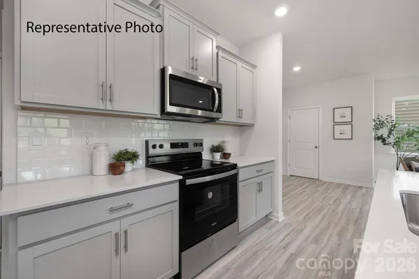 a kitchen with stainless steel appliances granite countertop white cabinets a sink a stove a microwave and wooden floors