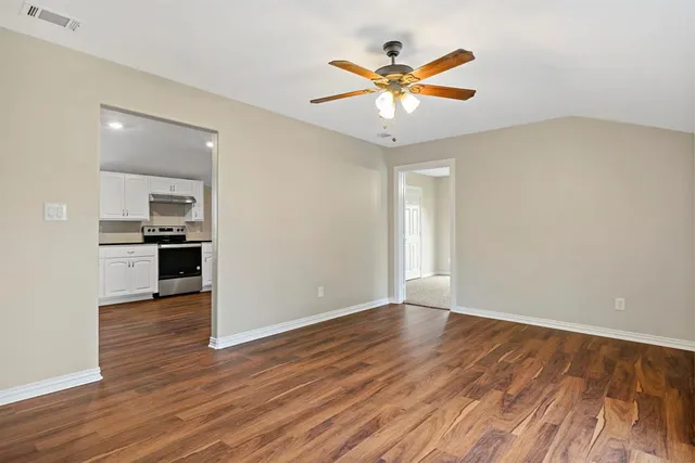 an empty room with wooden floor a ceiling fan and a kitchen