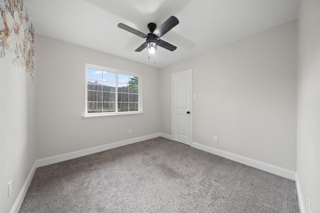 310 Valley Spring Drive Arlington, TX 76018 - Photo 19 of 24 Carpeted interior room featuring a multi-pane window, white trim, a solid white door with black hardware, and a ceiling fan with integrated lighting