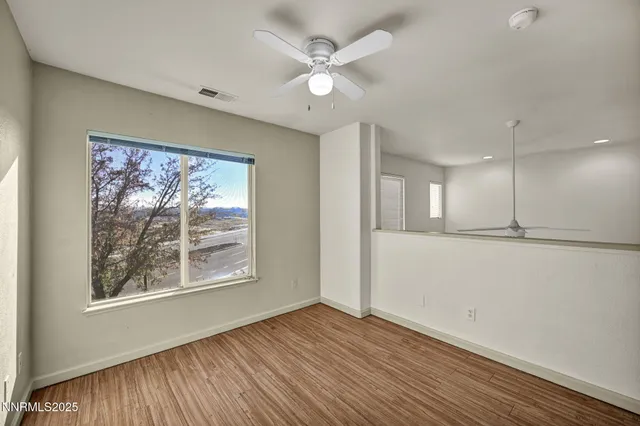 a view of an empty room with wooden floor and a ceiling fan