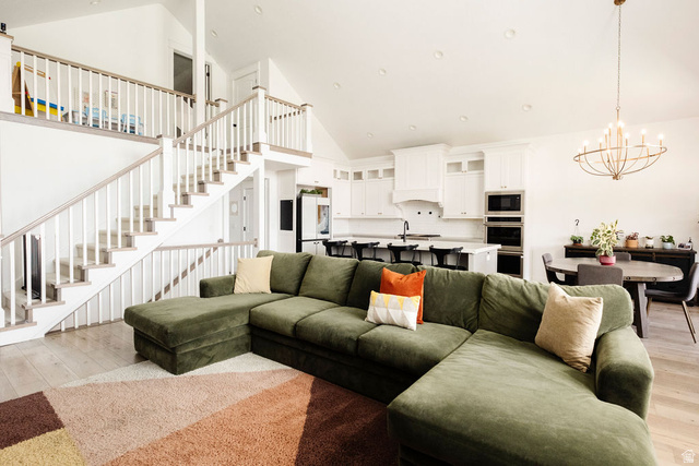 924 Country Lane Farmington, UT 84025 - Photo 20 of 91 Open concept living area with vaulted ceilings, featuring wood-finish flooring, a two-story staircase with white balusters, a kitchen with white cabinetry and built-in double ovens, and a dining area with a contemporary chandelier