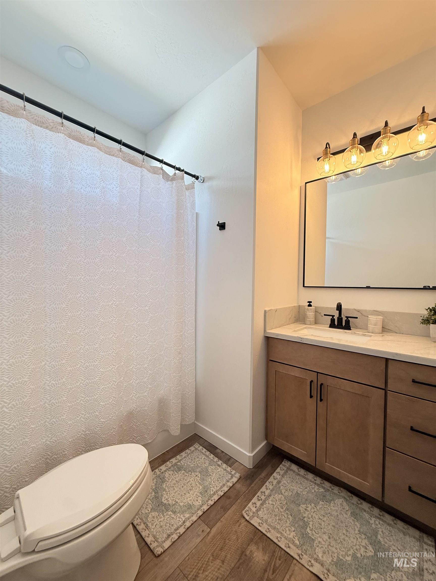 1220 Bronze Rupert, ID 83350 - Photo 23 of 30 Bathroom featuring wood-finish flooring, a contemporary vanity with a stone-look countertop, a rectangular sink with a matte black faucet, and a black-framed mirror illuminated by a four-bulb light fixture