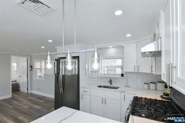 a kitchen with stainless steel appliances granite countertop a refrigerator a sink a stove and white cabinets with wooden floor