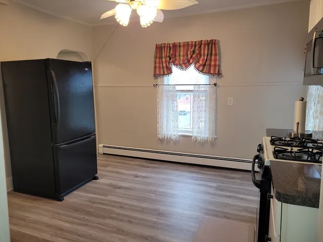 a view of a refrigerator in kitchen and an empty room with wooden floor