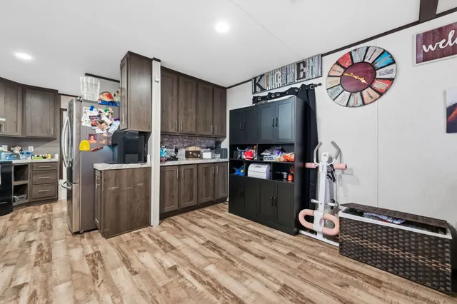 a kitchen with stainless steel appliances kitchen island granite countertop a refrigerator oven a sink dishwasher and wooden cabinets with wooden floor