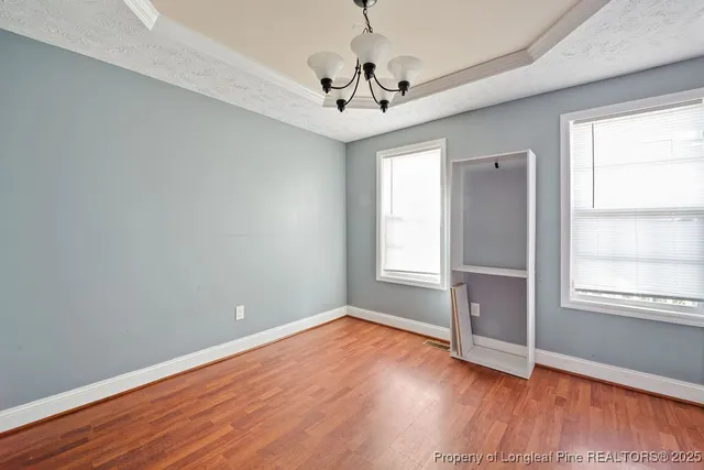 an empty room with wooden floor chandelier and windows