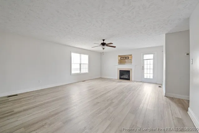 an empty room with wooden floor fireplace and windows