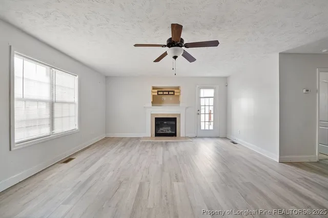 an empty room with windows fireplace and wooden floor