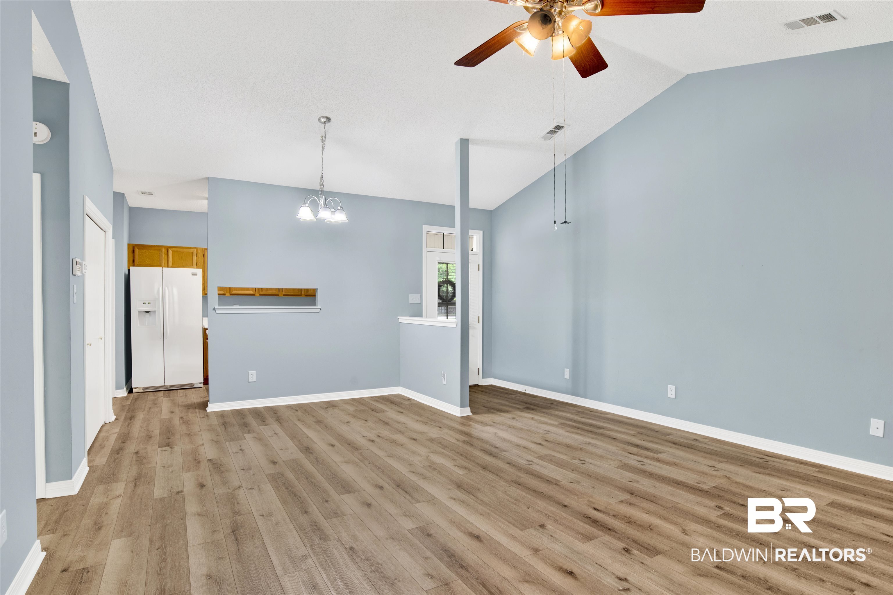 1258 Sutton Court, Unit 4 Mobile, AL 36609 - Photo 4 of 19 Unfurnished living room featuring visible vents, lofted ceiling, baseboards, light wood finished floors, and ceiling fan with notable chandelier