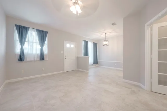 an empty room with chandelier fan and windows