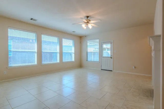 an empty room with chandelier fan and windows