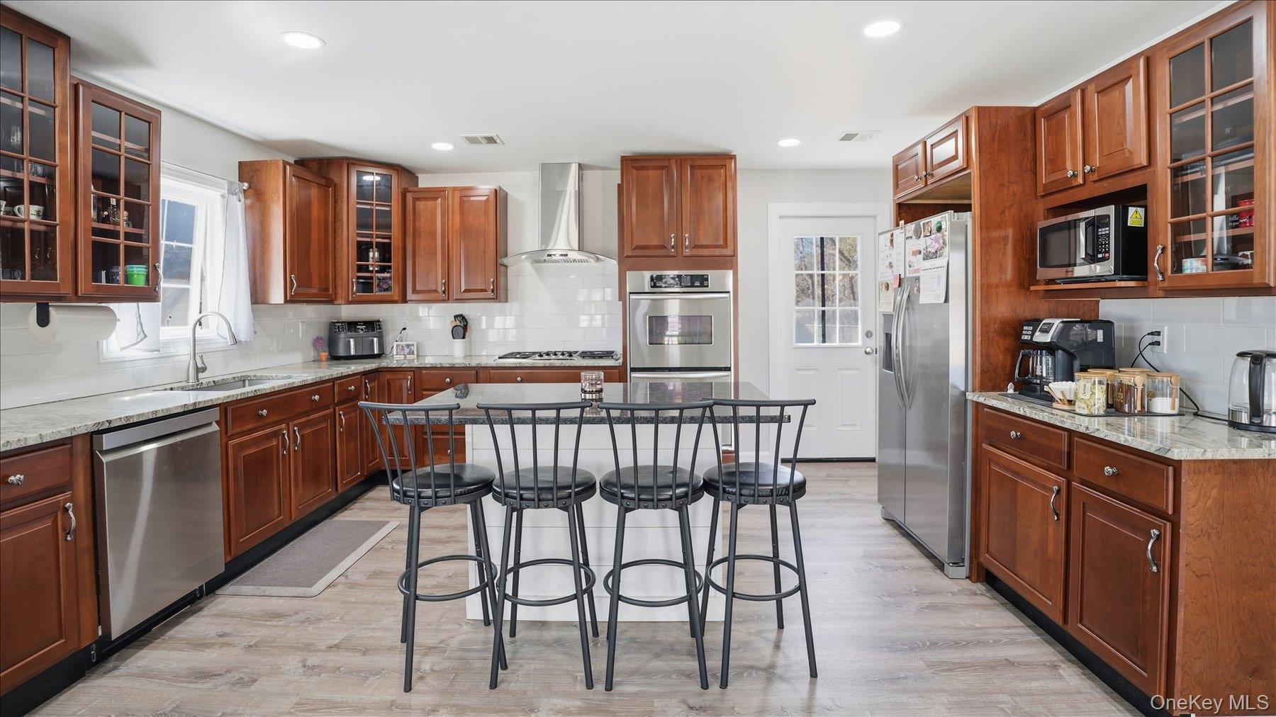 130 Beaver Dam Road Brookhaven, NY 11719 - Photo 14 of 30 Kitchen featuring glass fronted cabinets, light stone countertops, a breakfast bar area, stainless steel appliances, and a center island