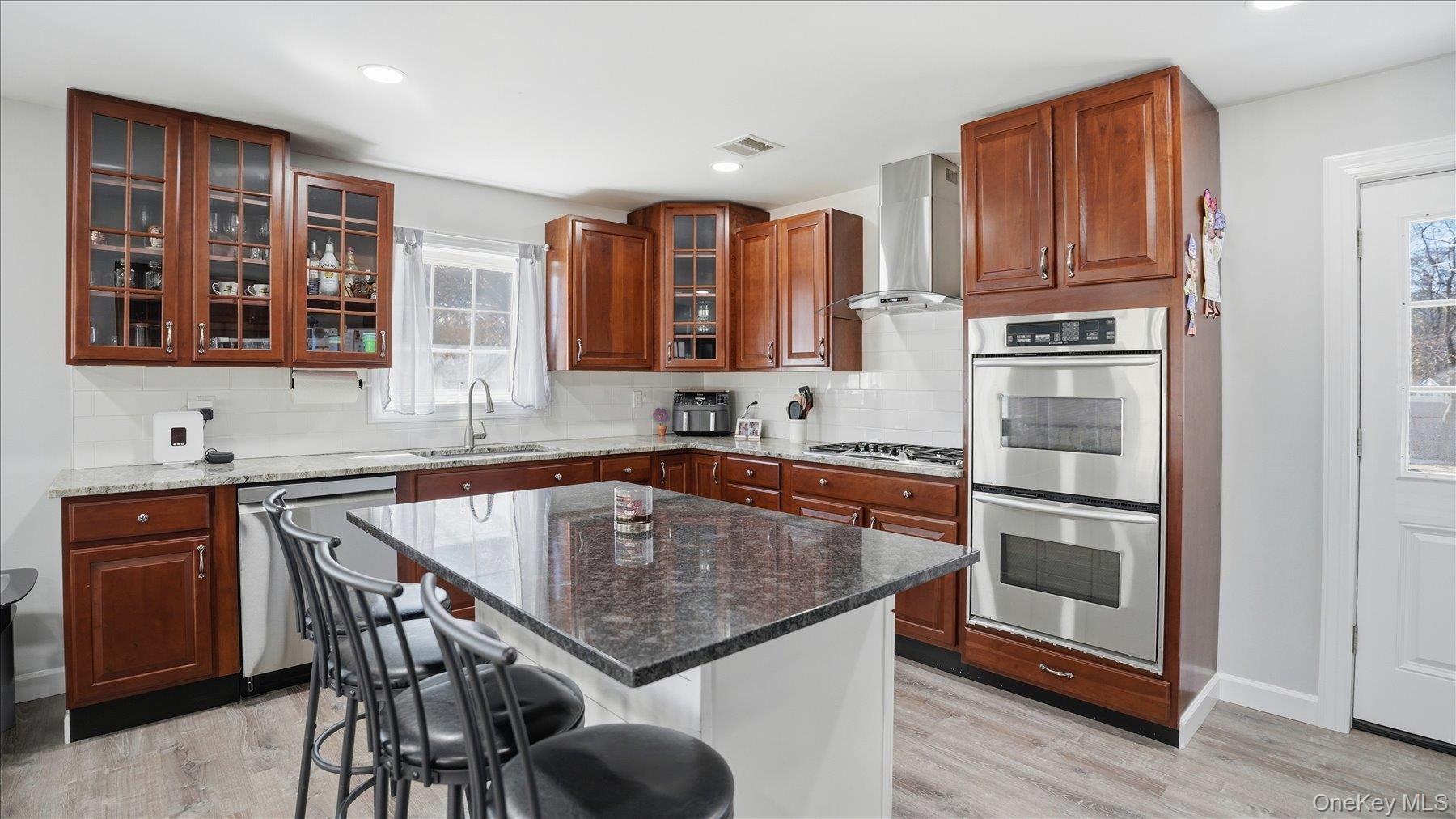 130 Beaver Dam Road Brookhaven, NY 11719 - Photo 15 of 30 Kitchen with dark stone counters, stainless steel appliances, light wood finished floors, a breakfast bar area, and a center island
