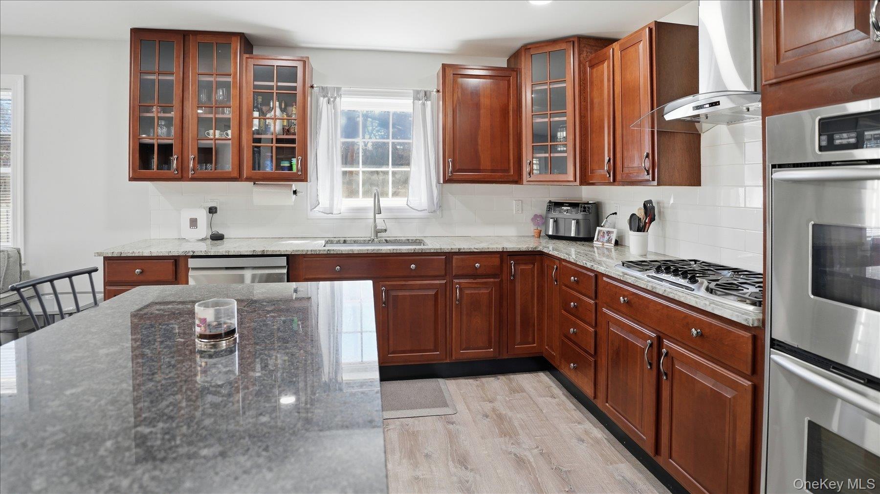 130 Beaver Dam Road Brookhaven, NY 11719 - Photo 16 of 30 Kitchen featuring glass insert cabinets, stainless steel appliances, dark stone countertops, light wood-style flooring, and tasteful backsplash