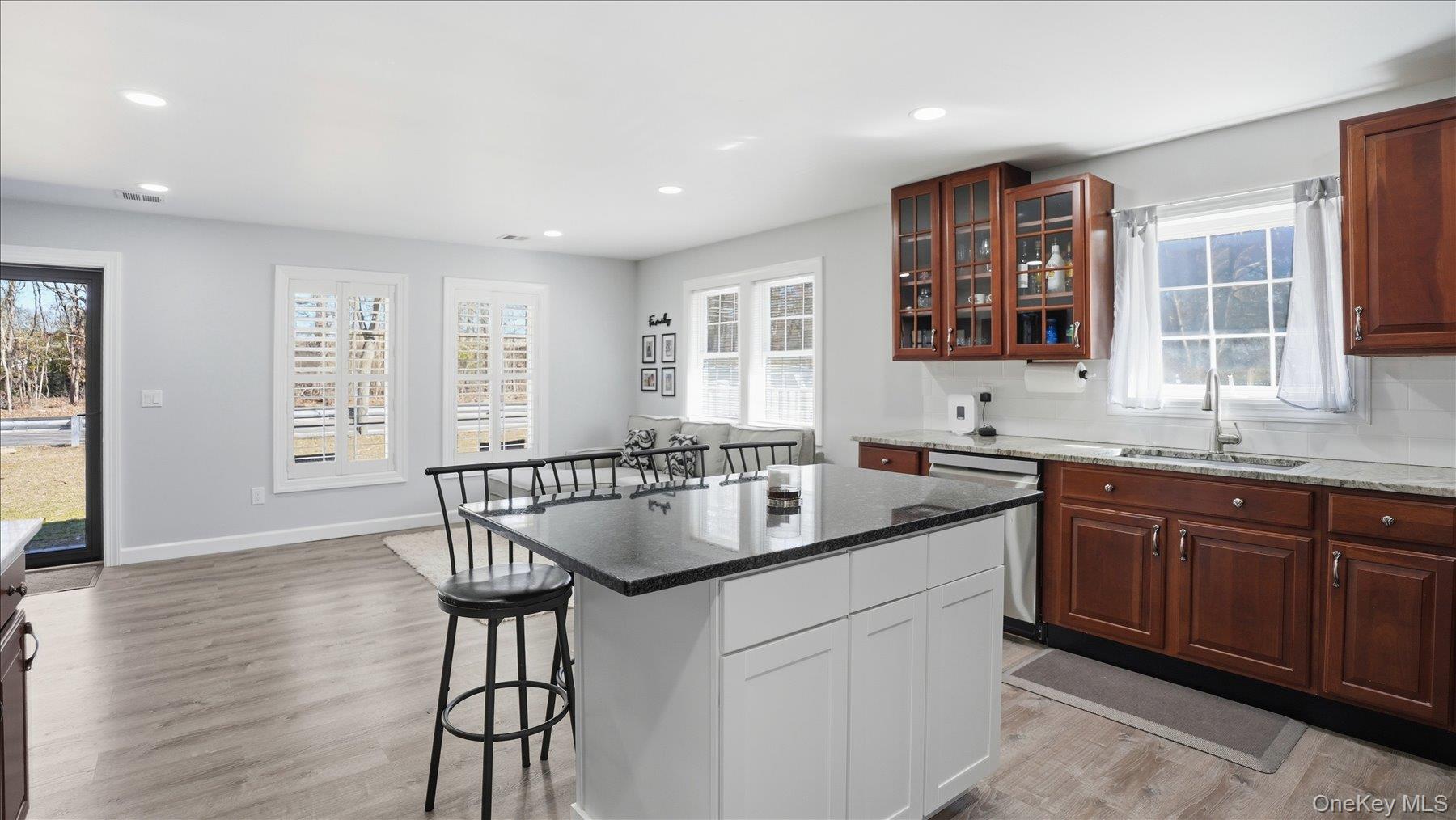 130 Beaver Dam Road Brookhaven, NY 11719 - Photo 18 of 30 Kitchen featuring two tone cabinets, dark stone countertops, a kitchen bar, glass insert cabinets, and light wood-style floors