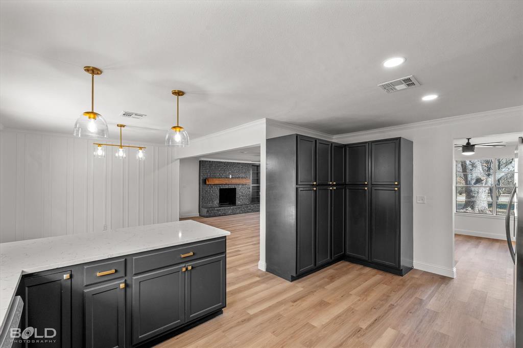 4136 Pines Road Shreveport, LA 71119 - Photo 11 of 38 Kitchen with a fireplace, light stone countertops, light wood-style flooring, dark cabinets, and decorative light fixtures