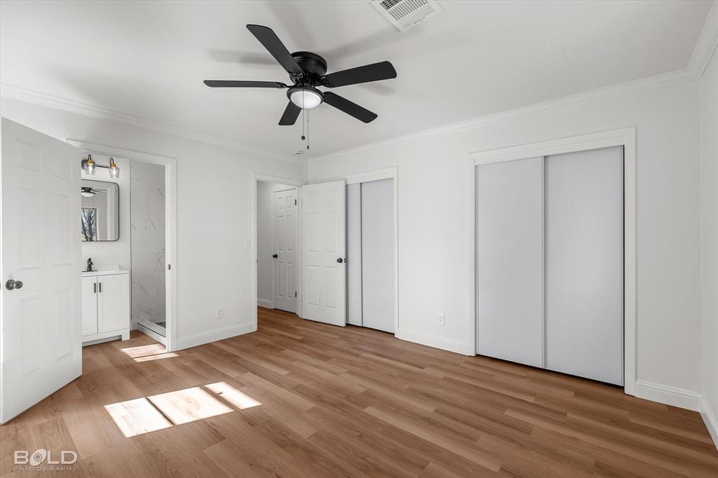 4136 Pines Road Shreveport, LA 71119 - Photo 21 of 38 Unfurnished bedroom with multiple closets, crown molding, connected bathroom, light wood-style flooring, and a ceiling fan