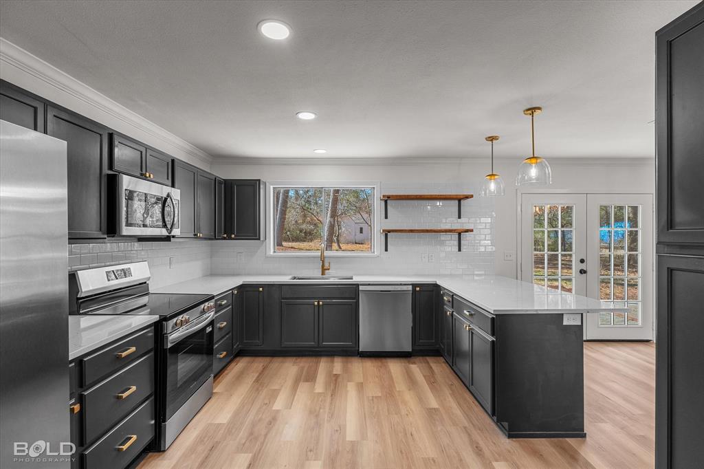 4136 Pines Road Shreveport, LA 71119 - Photo 8 of 38 Kitchen with a peninsula, hanging light fixtures, stainless steel appliances, open shelves, and light wood-style flooring