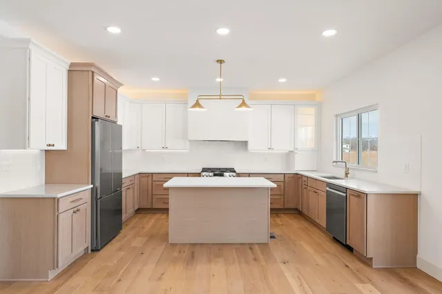 a kitchen with stainless steel appliances granite countertop a white cabinets a sink dishwasher a refrigerator and a stove with wooden floors