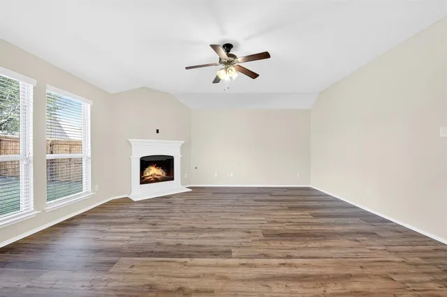 a view of an empty room with wooden floor fireplace and a window